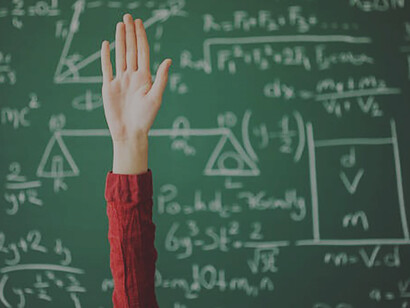 A student raising their hand against a green board in a classroom challenges the tenets advocated by Rousseau