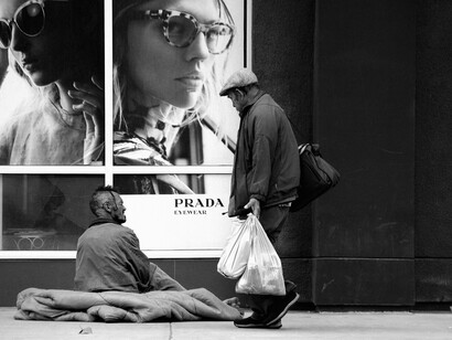 Un homme vit dans la rue au pied d'un magasin Prada illustrant les inégalités croissantes