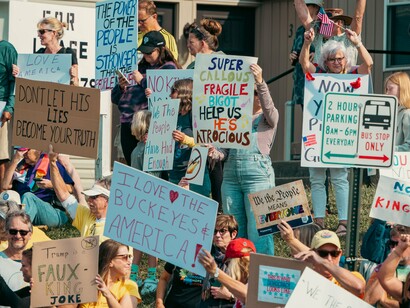 Protesters holding colourful signs and raising their voices in the street, symbolizing resistance to the erosion of democratic values
