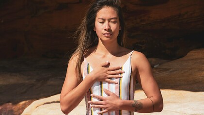 A woman practicing mindful breathing with her hands resting on her chest and abdomen, representing the calming influence of conscious breath on the nervous system
