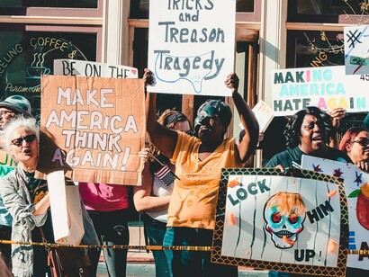 A diverse crowd raising hand-painted anti-Trump signs in public protest, representing growing resistance to political division and the erosion of democratic trust