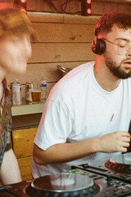 A bespectacled DJ spins mesmerizing beats, while the man beside him dances with unbridledly