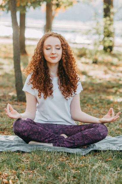 Woman practicing yoga on the grass in a park, looking healthy and relaxed