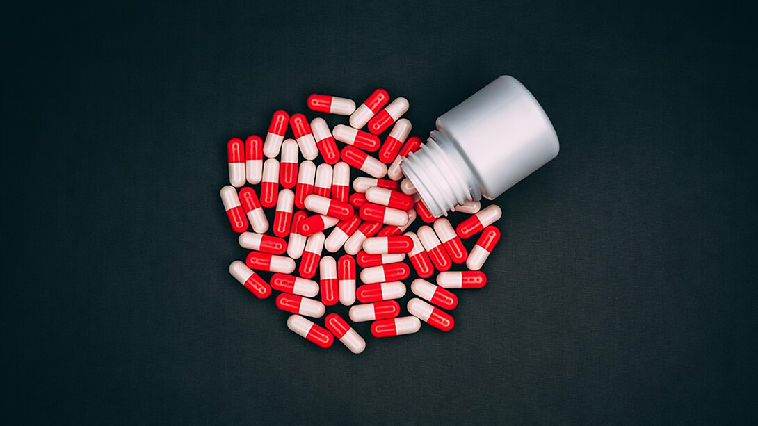 High-angle view capturing red-and-white capsule drugs cascading from a small pill bottle