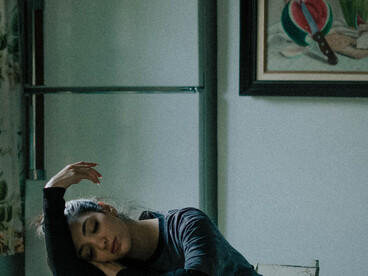 A contemplative young woman seated alone in a dim apartment, symbolising urban loneliness and emotional pressure on women in the Middle East