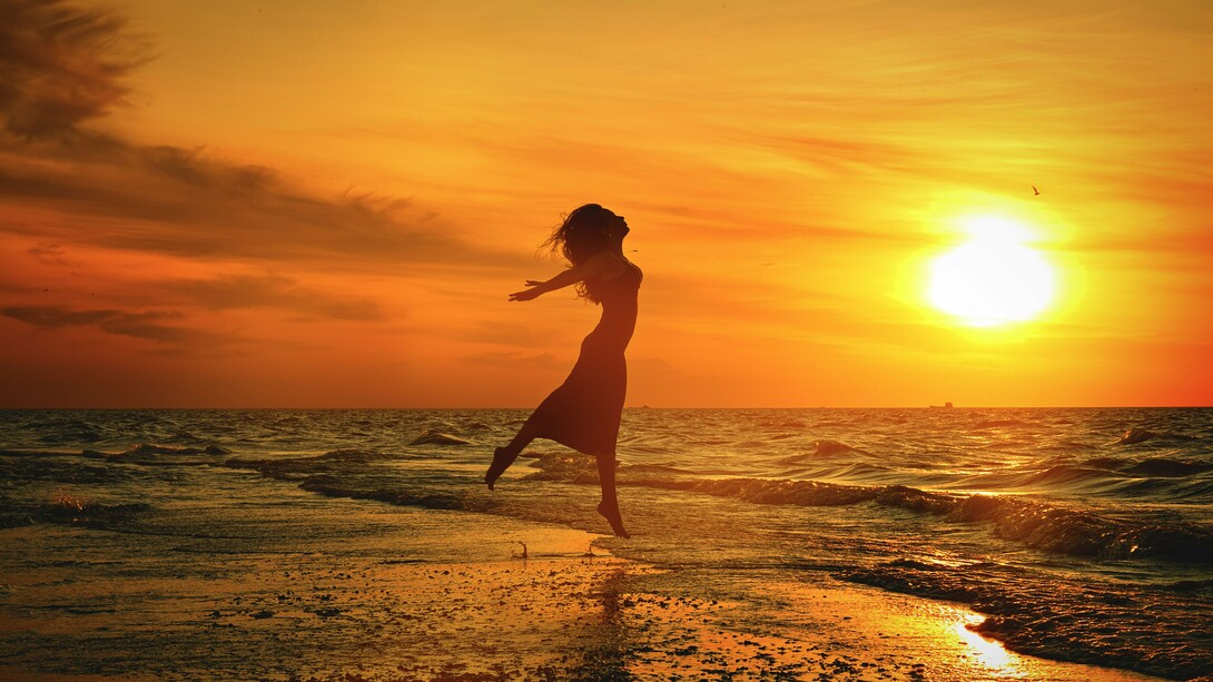Em silhueta contra o céu dourado, uma mulher salta diante do mar ao pôr do sol. A imagem traduz a sensação de liberdade e de abertura para novas possibilidades que atravessa o texto