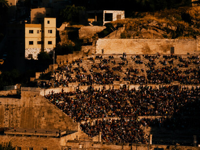 A bustling Roman theatre at sunset, filled with people and reflecting the vibrant atmosphere of local culture and community life