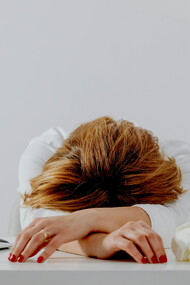 A female writer resting her head on the table beside a laptop, looking anxious and depressed