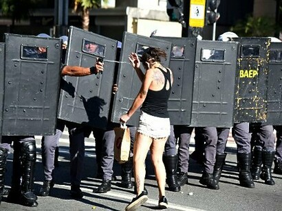 O gesto de resistência diante da barreira policial sintetiza um momento de forte tensão nas ruas. Ao discutir democracia, poder, capitalismo e formas de dominação, o texto convida o leitor a pensar os conflitos que atravessam as sociedades atuais