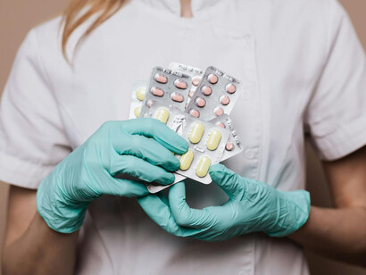 Mujer con uniforme médico y guantes quirúrgicos sostiene blísteres de medicamentos