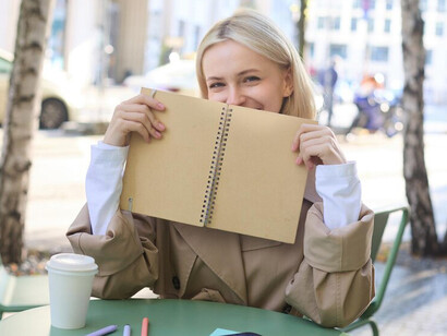 A cheerful young blonde woman relaxes at an outdoor café, journaling in her gratitude notebook as she embraces the serenity of meditation
