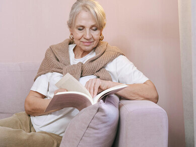 Older woman peacefully reading at home while sitting on a cozy couch with glasses on