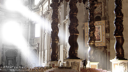 The ancient Solomonic columns mounted above the balcony, positioned in the upper-right background against the wall in St. Peter's Basilica, Vatican City, Italy
