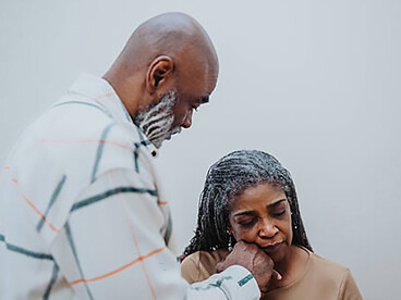 A senior man gently comforts his wife, holding her hand as she cries during her illness