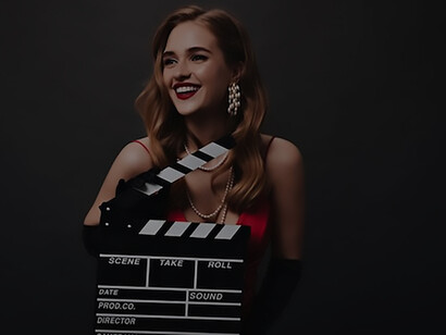A sophisticated woman in a striking red dress strikes a poised pose while holding a classic clapperboard against the backdrop of a sleek black setting, embodying Hollywood glamour and stardom