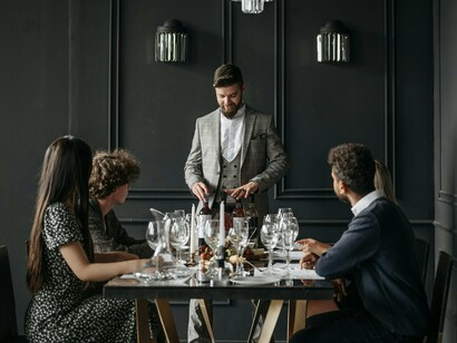 A sommelier presenting premium wines to diners, representing the role of prestige and curated experiences in shaping food value