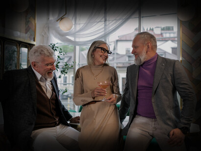 Two older gentlemen and a woman talk together, having drinks