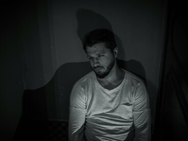 Um homem sentado num quarto escuro, envolto em sombras e silêncio. Como o protagonista, parece esmagado pelo peso invisível dos dias que não avançam
