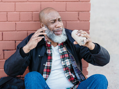 A middle aged black black sitting on the street, about to drink from a cup