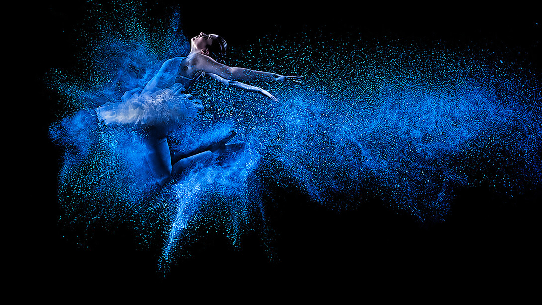 A young dancer leaps gracefully through a cloud of vibrant blue powder, creating a striking display of movement and artistic expression