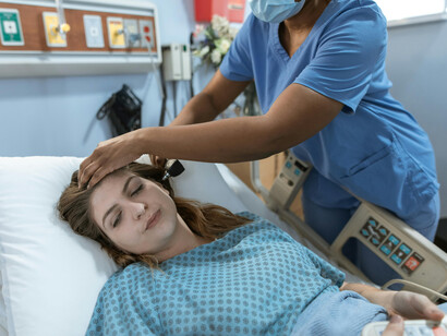 A nurse examines the patient's ear. The woman seems distressed by pain; the nurse seems careful in her avaliation