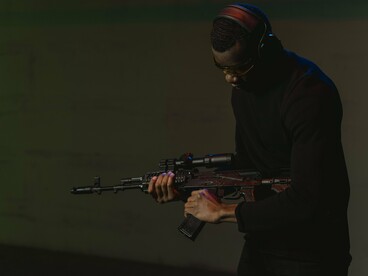 Atirador segura uma Kalashnikov AKM durante exercício de precisão. O texto questiona a utilização da força como resposta aos conflitos políticos