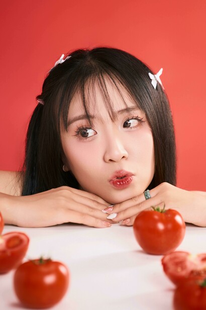 A whimsical, playful portrait of a woman posing with tomatoes on a vibrant red background