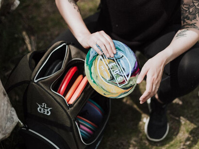 A person sitting on a tree stump with a backpack and several disc golf discs
