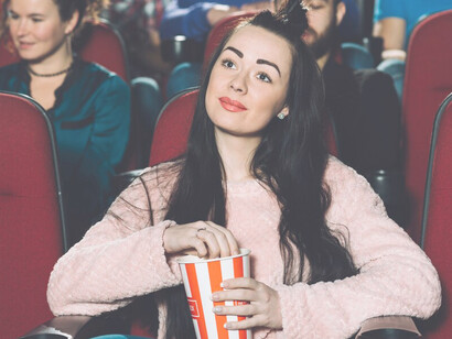 A brunette woman savoring popcorn at the cinema, experiencing the magic of the big screen