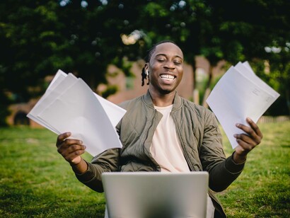 A man smiling and celebrating his success in a park while holding papers