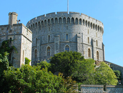 View of Windsor Castle’s Round Tower in England, UK, showing the gray stone structure crowned with the royal flag against a bright blue sky