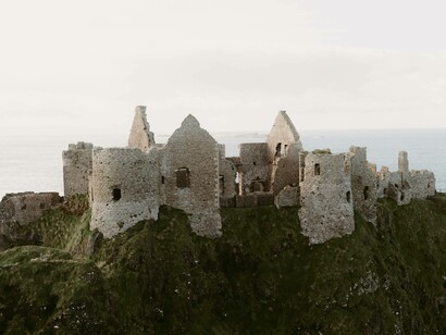 Old medieval ruins of Dunluce Castle on the ocean coast under light grey skies in Northern Ireland 