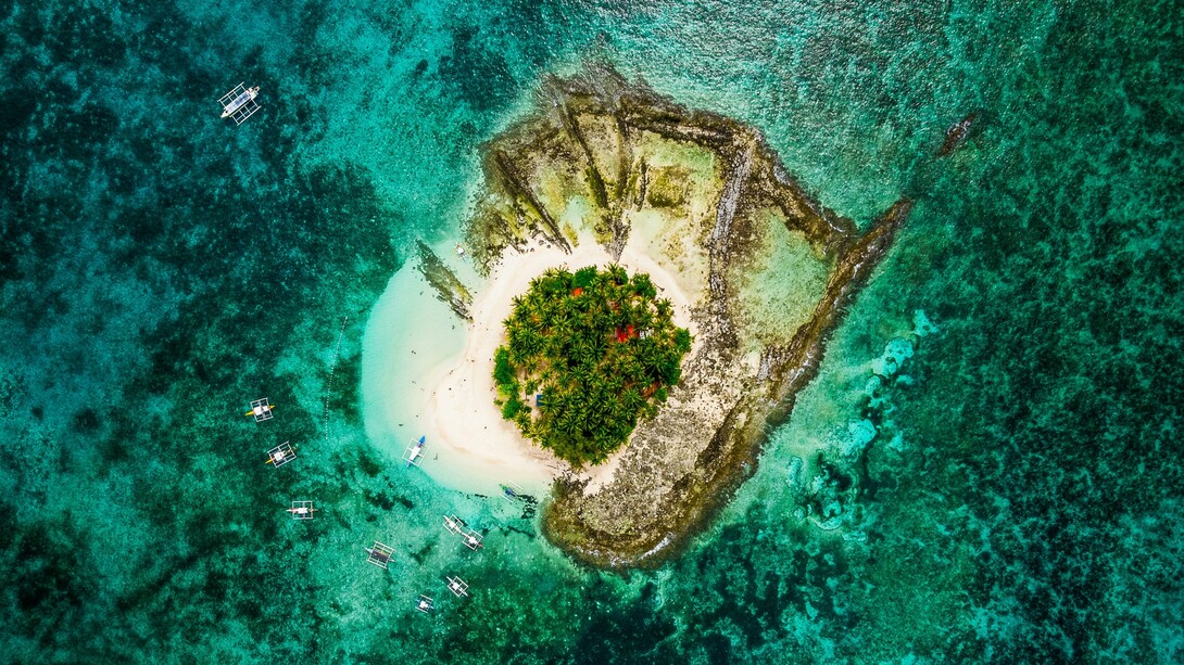 An aerial view of Guyam Island in Siargao, signifying the timeless allure of small islands surrounded by vast seas