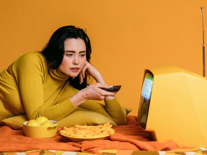 Mulher se distrai em frente à televisão. A arte é terapia. Achei conforto misturado na nostalgia de épocas que já vivi, juntamente com meus personagens favoritos em situações cômicas. Ao fugir um pouquinho, mesmo que por uns minutos daquela angústia da realidade, comecei a me reconectar comigo mesma, aquela antiga eu, a menina, a adolescente, a mulher, aquela que sabe que o mundo é grande demais, e que quer experimentar e viver as melhores que ele tem para oferecer