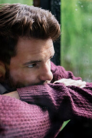 A heartbroken man, looking through the window on a rainy day, waiting for his lover to come back home