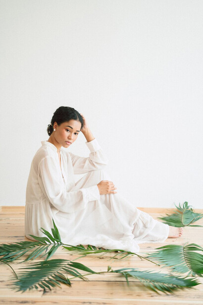 Dressed in a long white gown, a woman sits in an empty room, reflecting the essence of sustainable, circular, and biodegradable fashion