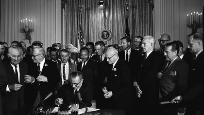 El presidente Lyndon Johnson firma la Ley de Derechos Civiles el 2 de julio de 1964 en presencia de Martin Luther King. El proyecto de ley fue presentado en junio de 1963 por el presidente John F. Kennedy, si bien fue frenado por el Senado. Cinco meses después Kennedy fue asesinado y asumió la presidencia Lyndon B. Johnson, quien finalmente firmaría la ley 10 meses más tarde