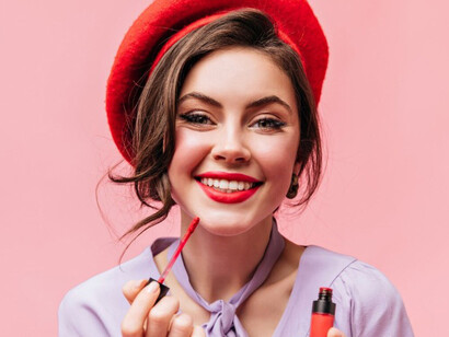 Close-up of a smiling woman applying red lipstick, symbolizing emotional comfort and the lipstick effect during economic uncertainty