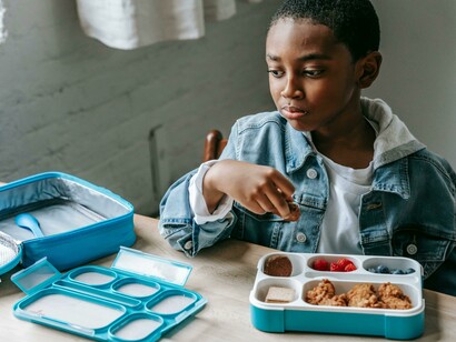Joyful Black schoolboy talking with a girl friend over lunch, featuring a colorful kids’ lunchbox