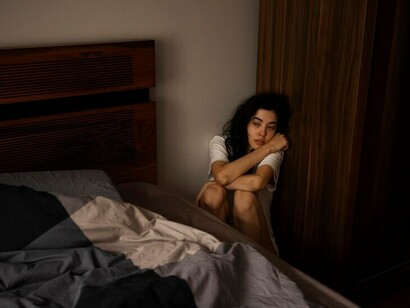 A young woman sitting on the floor beside her bed, overwhelmed by anxiety