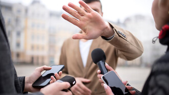 A close-up image of a reporter conducting an interview, with a person gesturing to block the camera