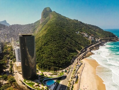 A vista aérea revela o encontro entre o mar, a faixa litorânea, a vegetação dos morros e a ocupação urbana do Rio de Janeiro. Na paisagem carioca, a proximidade física entre áreas valorizadas, comunidades e belezas naturais não elimina as profundas diferenças sociais que estruturam o território