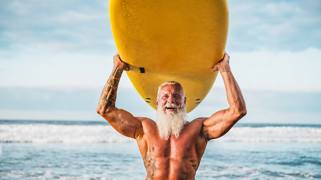 Happy elderly man surfing on a longboard, embracing an active lifestyle and proving that age is no barrier to adventure