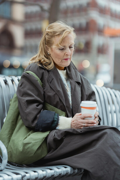 Melancholic woman sitting alone on an urban bench, holding a takeaway coffee and lost in thought amid the city around her