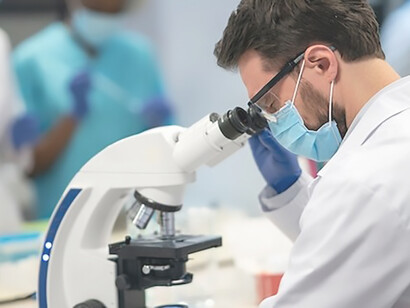 Within the laboratory, a male scientist is immersed in his work, utilizing a microscope to conduct meticulous research and contribute to scientific advancements