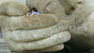 A child sits inside the giant hand of a face statue