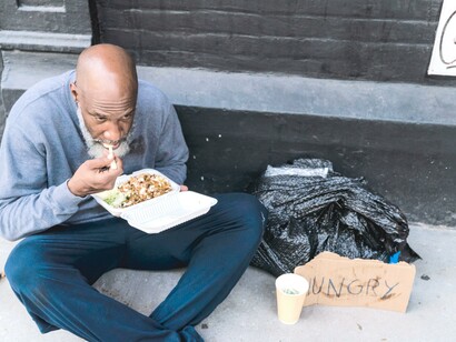 Morador de rua comendo na calçada