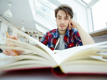 A person dealing with academic stress and OCD, sitting in the library, their head in their hands in frustration