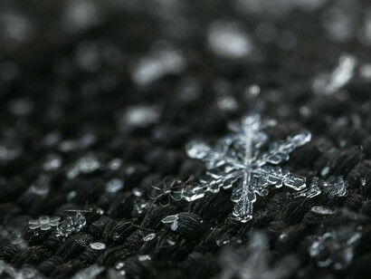 A single, perfectly formed snowflake stands out against a blurred background of other ice crystals, embodying the detailed artistry often associated with winter's frozen precipitation