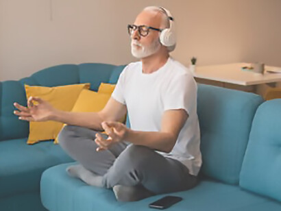 Mature senior man sitting on floor practicing guided meditation at home, relaxing body and mind concept